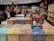 A bustling candy store with a colorful display of individually wrapped chocolates arranged in open bins. Shoppers are selecting candies from the wide variety, while others browse the shelves filled with sweet treats. The store has a warm and inviting atmosphere.