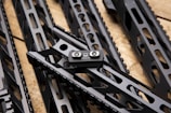 Several sleek, black metallic handguards featuring cut-out designs are arranged in a diagonal pattern on a wooden surface. A small metal component labeled 'STRIKE M MADE IN USA' is prominently attached to one of the handguards.
