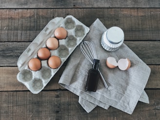 Fresh eggs, milk cartons, red meat cuts, and grocery items arranged on a rustic wooden table.