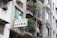 A multi-story building with balconies adorned with potted plants and laundry. Several air conditioning units are installed on the walls. A sign in both English and Chinese characters is displayed, indicating the presence of a medical practice.