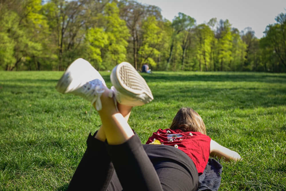 woman in black pants and red shirt lying on green grass field during daytime