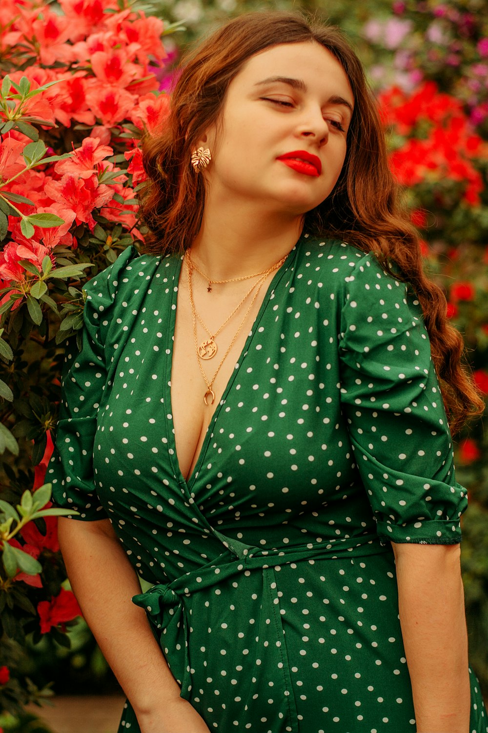 woman in green dress standing beside red flowers