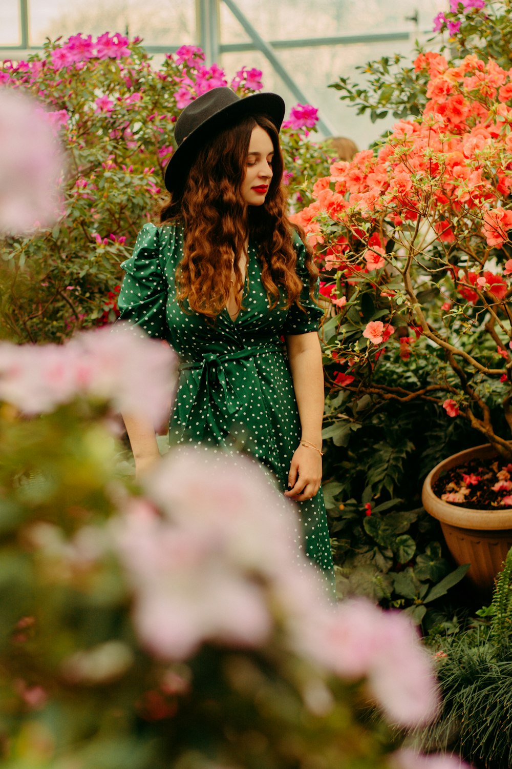 Mujer con vestido verde de pie cerca de las flores rojas