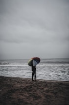 person holding red yellow and green umbrella walking on beach during daytime