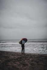 person holding red yellow and green umbrella walking on beach during daytime