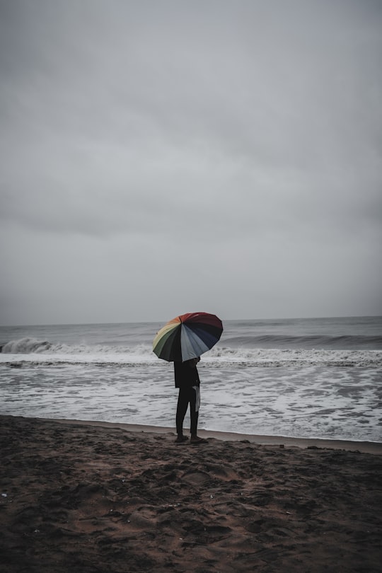 person holding red yellow and green umbrella walking on beach during daytime in Alappuzha India