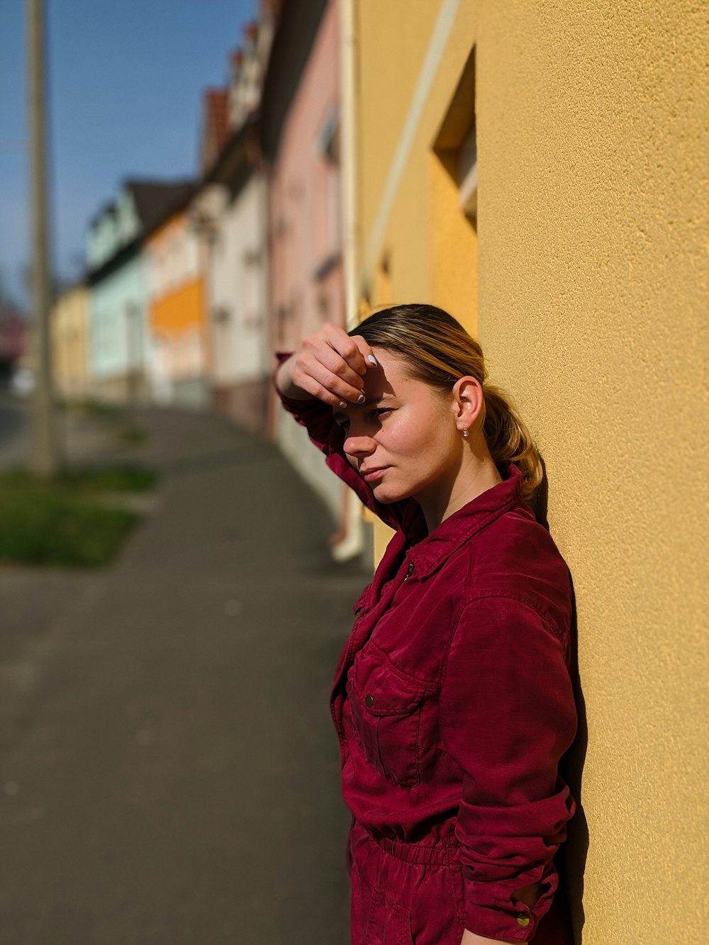 赤い長袖シャツを着た女性で、黒いフレームの眼鏡をかけ、昼間、黄色い壁のそばに立っている