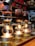 Several siphon coffee makers are aligned on a countertop, each with a base heater illuminating the bottom glass chambers. The upper chambers are filled with coffee grounds and water, creating a rich, aromatic brew. The warm glow from the lights contrasts with the dark liquid, creating a cozy and inviting ambiance.