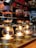 Several siphon coffee makers are aligned on a countertop, each with a base heater illuminating the bottom glass chambers. The upper chambers are filled with coffee grounds and water, creating a rich, aromatic brew. The warm glow from the lights contrasts with the dark liquid, creating a cozy and inviting ambiance.