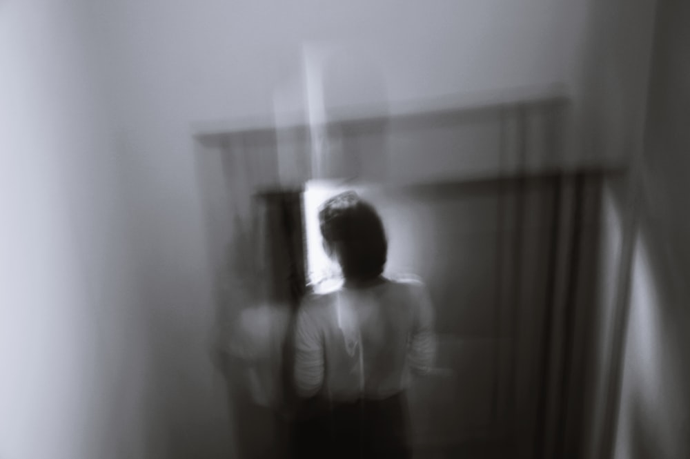 grayscale photo of woman in white shirt standing near window