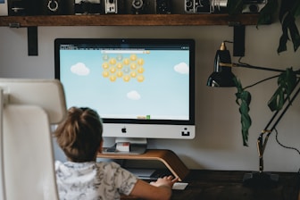 girl in white and blue floral shirt sitting on chair in front of silver imac