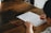 A person is writing on a worksheet titled 'Subordinate Clauses' placed on a wooden table. The individual holds a red pen and is filling in answers. A red pen cap lies nearby on the table.