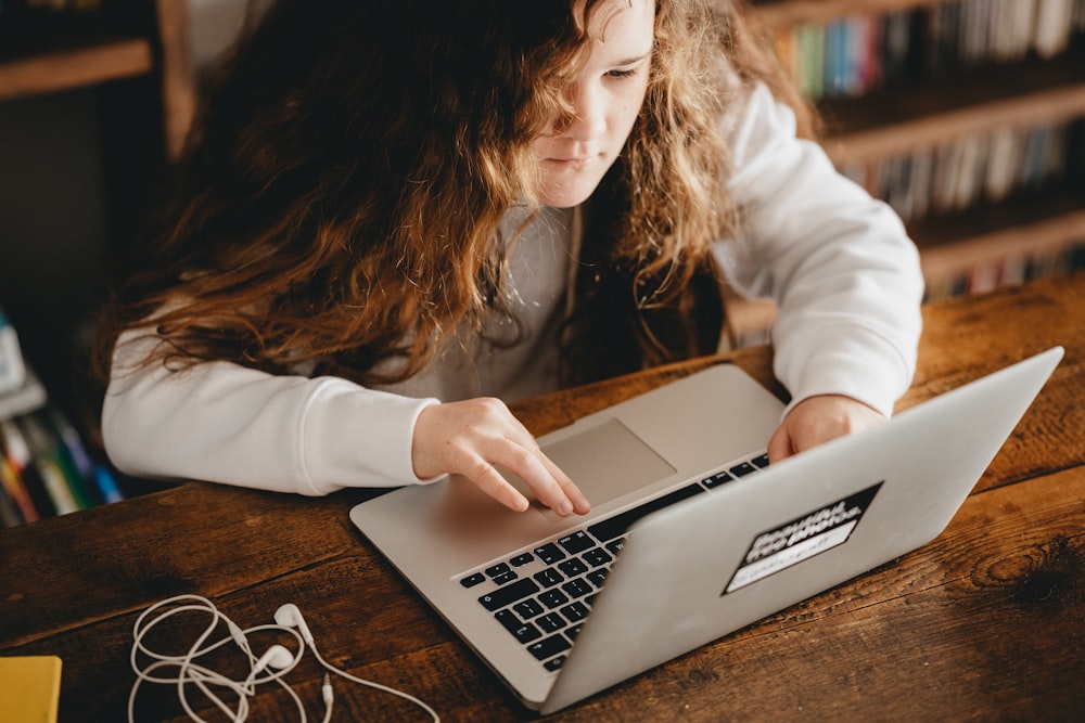 woman in white long sleeve shirt using macbook air on brown wooden table