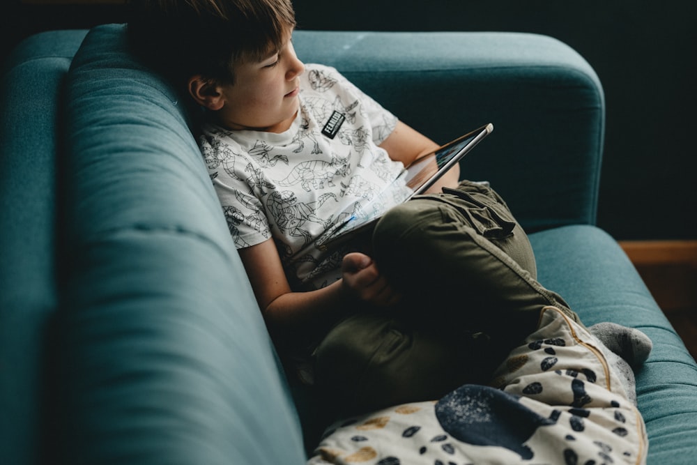 boy in white and black crew neck t-shirt and gray pants sitting on black couch