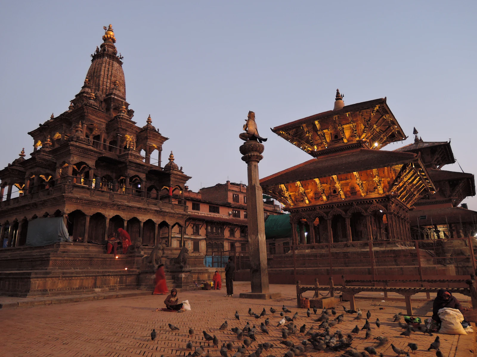 Patan Durbar Square at dusk: the stone Krishna Mandir, a Garuda on its column and a lamplit pagoda roof