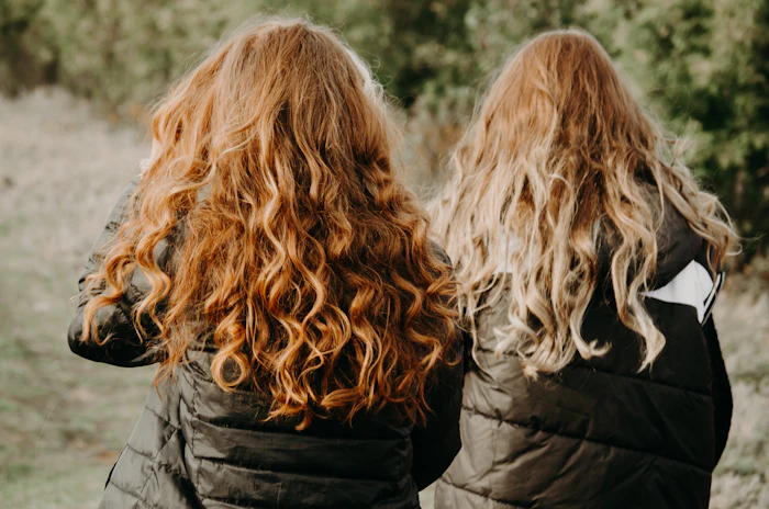 Two people seen from behind, one with long copper curls and one with blonde curls