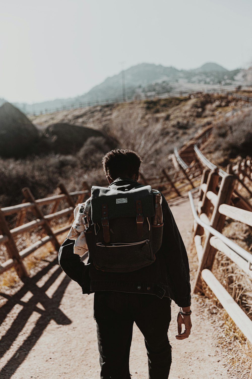 man in black jacket carrying backpack standing on brown wooden fence during daytime