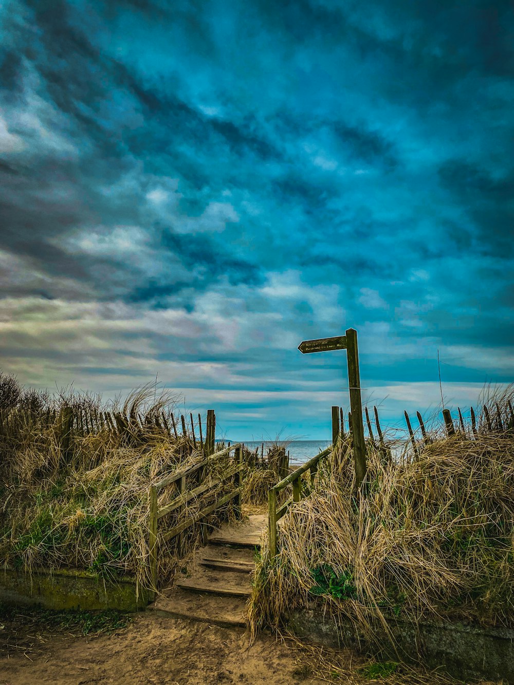 brown wooden fence on green grass field under blue sky and white clouds during daytime