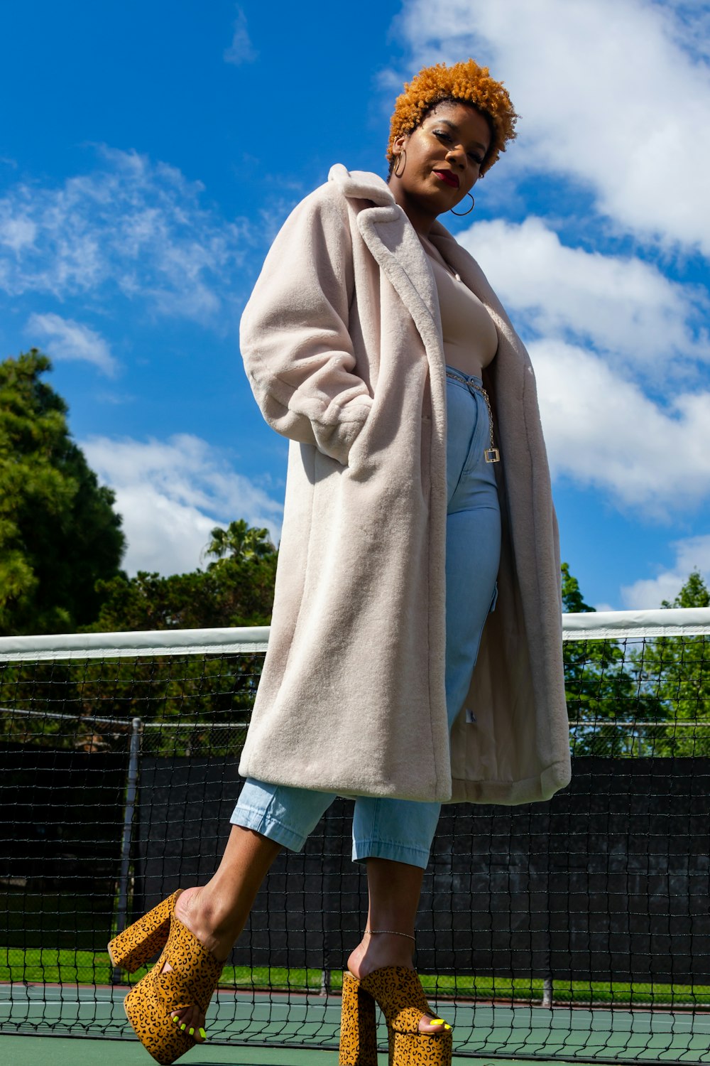 woman in brown coat standing near fence under blue sky during daytime