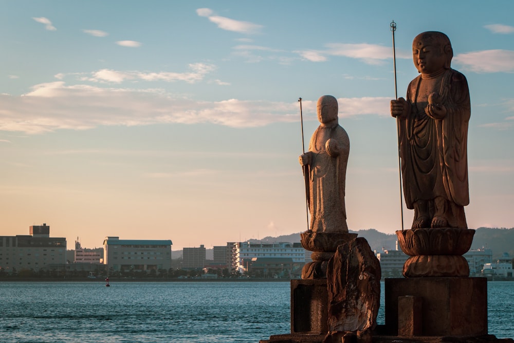 gold statue of man near body of water during daytime