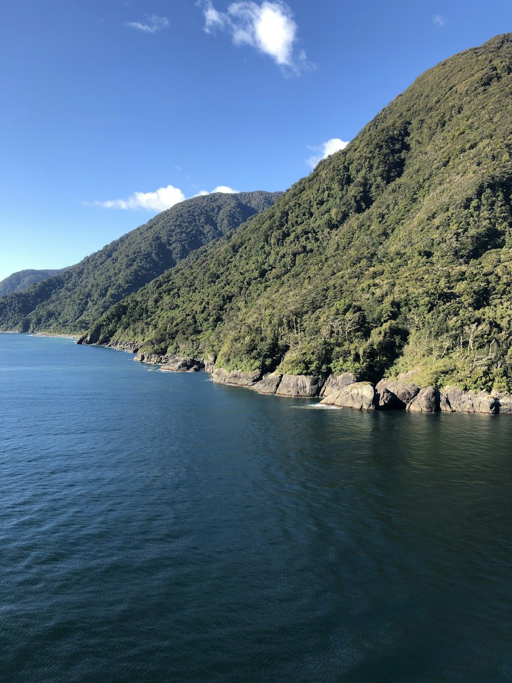 people swimming on blue sea near green mountain under blue sky during daytime