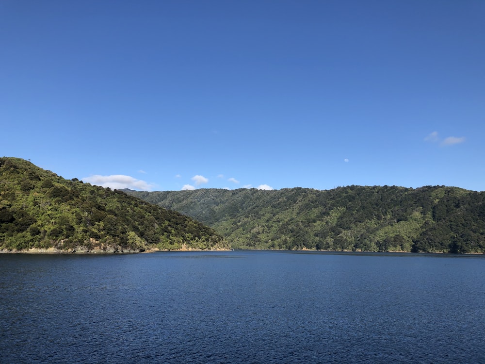 blue lake surrounded by green trees and mountains under blue sky during daytime