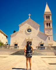 woman in black and white dress standing in front of white concrete church during daytime