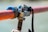 Close-up of a metal clamp securing a red rod, with visible blue padding for protection and a rope tied around it. The background is blurred, creating a shallow depth of field effect.