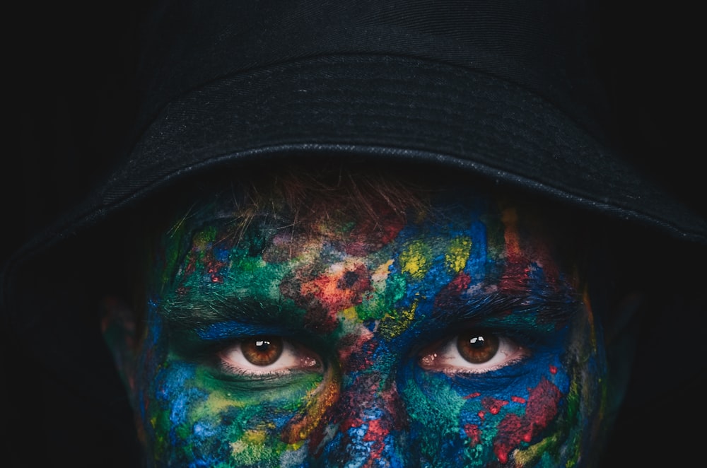 person in black hat with green blue and black face paint