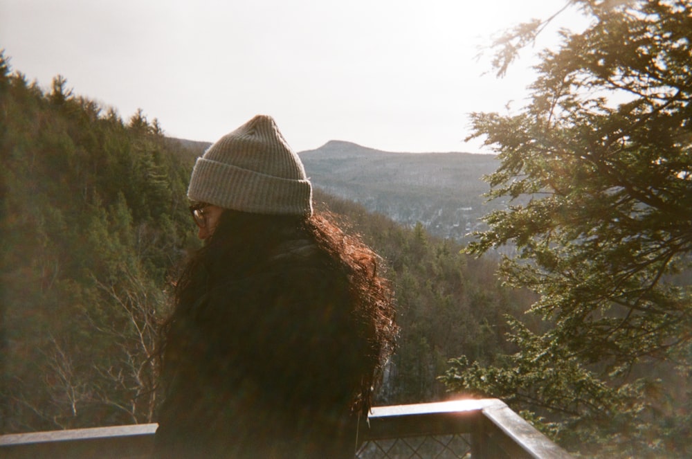Mujer con chaqueta marrón y gorra de punto blanca de pie en el balcón durante el día