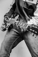 A person wearing a jacket and jeans is playing an electric guitar. The focus is on the hands, the guitar, and the lower part of the body. The image is in black and white, giving it a classic and timeless feel.