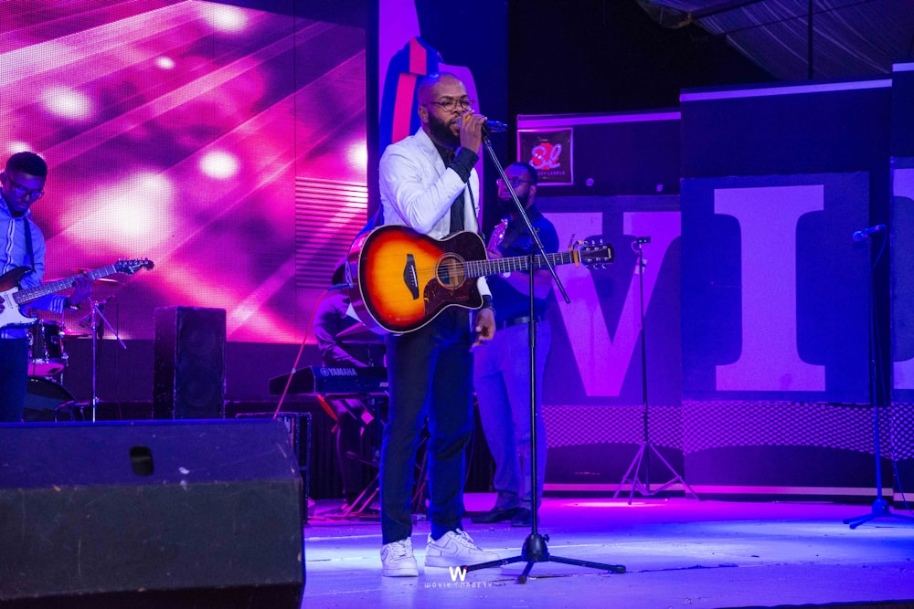 man in white dress shirt playing guitar on stage