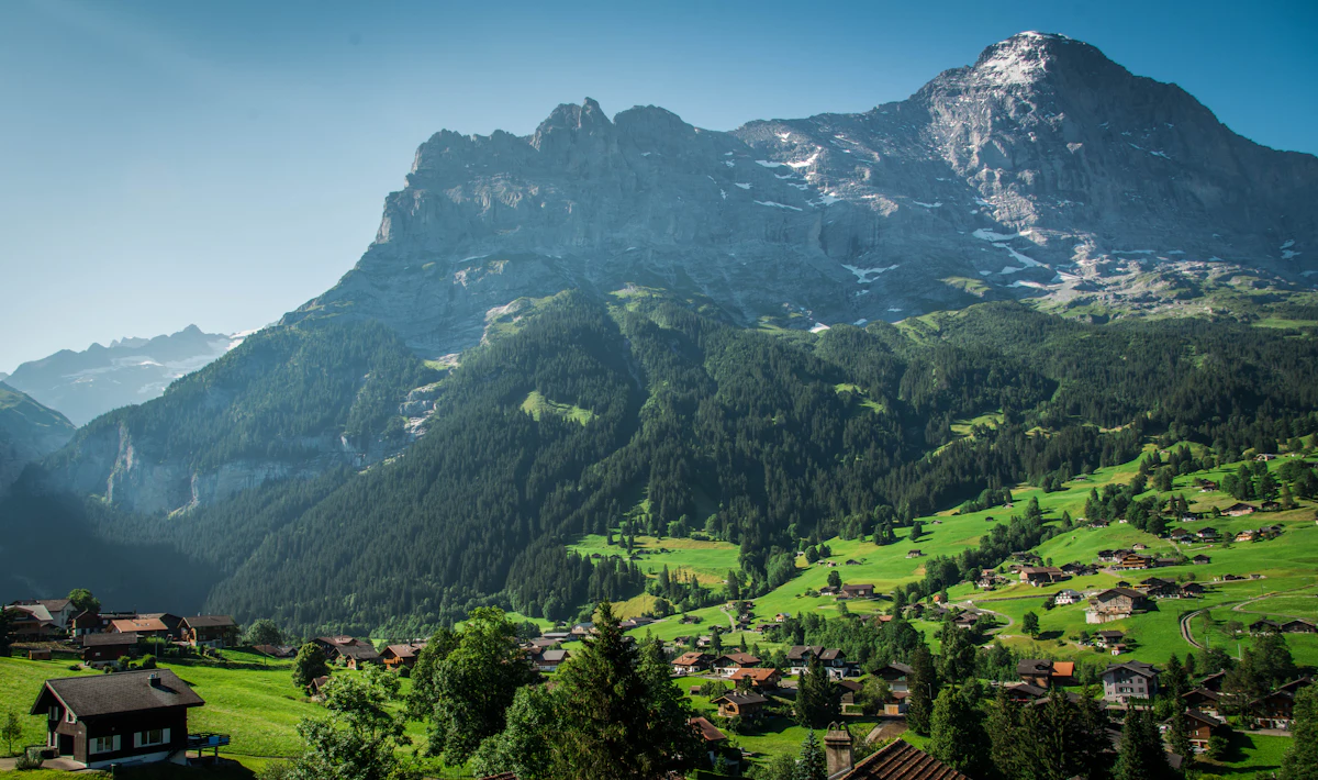 A huge grey rock wall above the forests and chalets of Grindelwald on a summer day