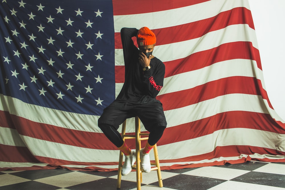 Homme en veste et pantalon en cuir noir assis sur une chaise près du drapeau de l’Amérique