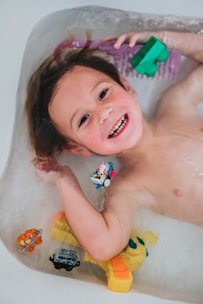 A cheerful child playing with colorful bath toys surrounded by gentle kid's skincare products.
