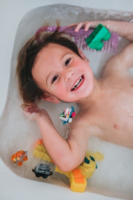 A cheerful child playing with colorful bath toys surrounded by gentle kid's skincare products.
