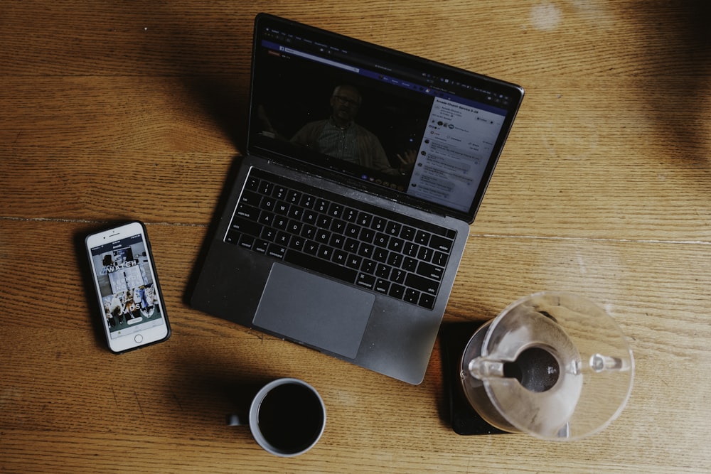 macbook pro beside white ceramic mug on brown wooden table