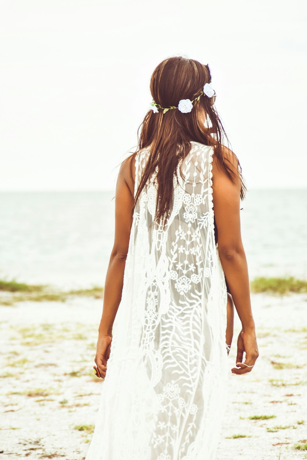 낮 동안 해변에 서 있는 흰색 민소매 드레스를 입은 여자