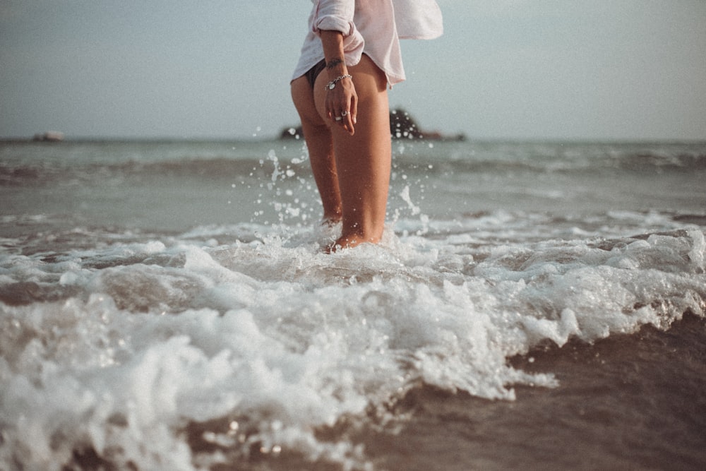 woman in white shirt and blue denim shorts standing on sea shore during daytime