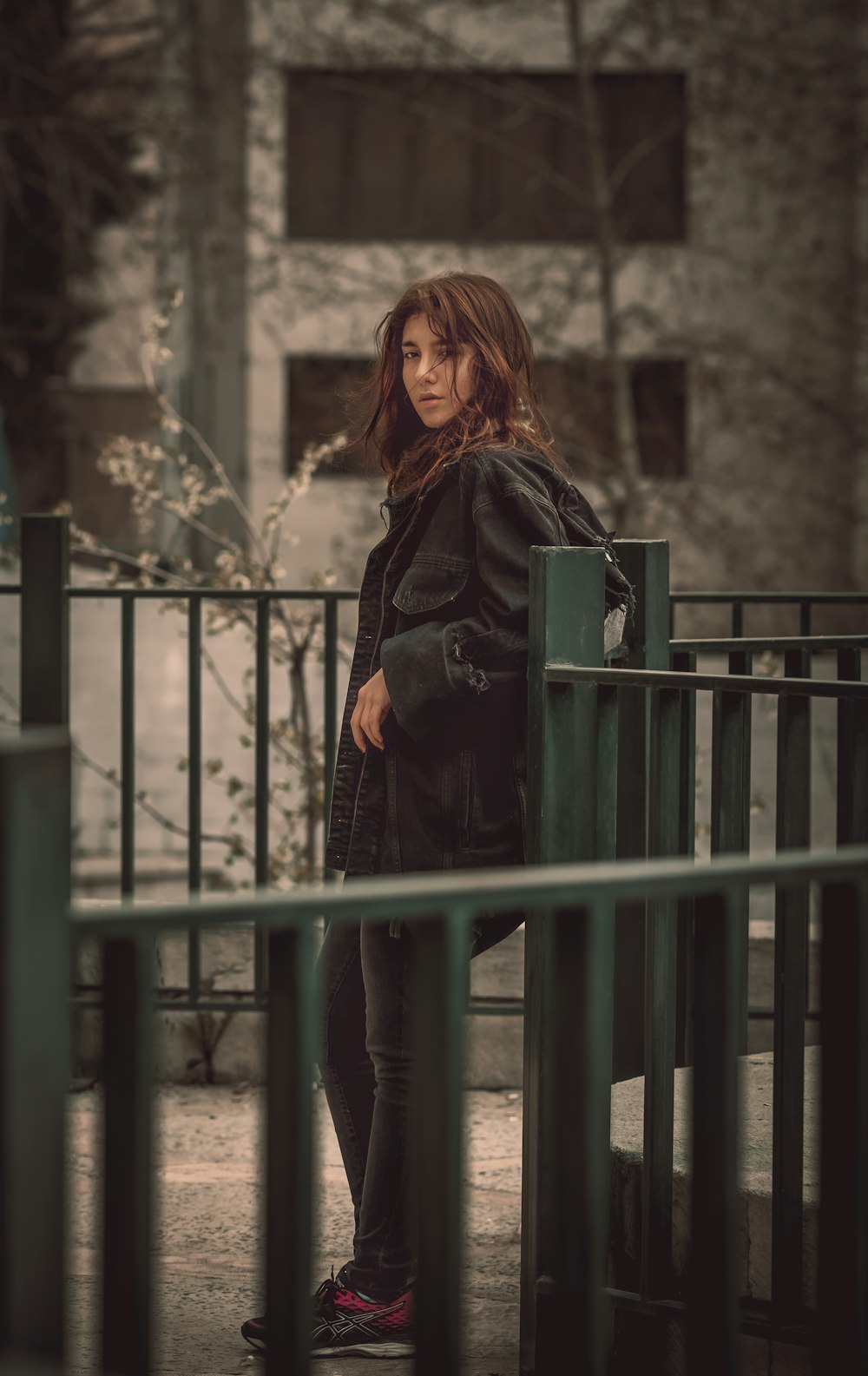 woman in black jacket standing beside blue metal fence during daytime