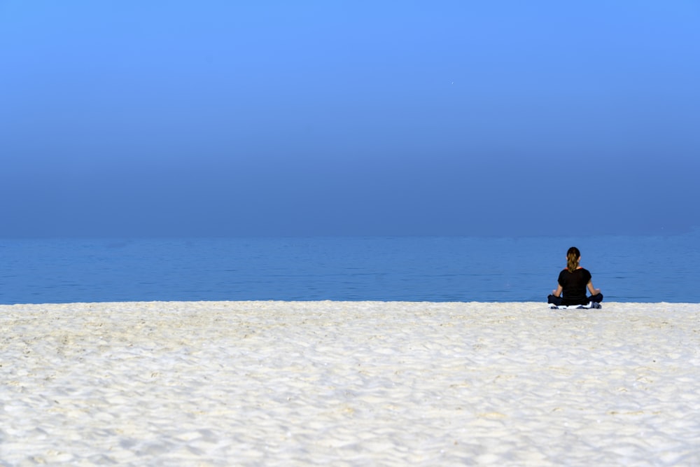 昼間、白い砂浜に座る黒いシャツの女性