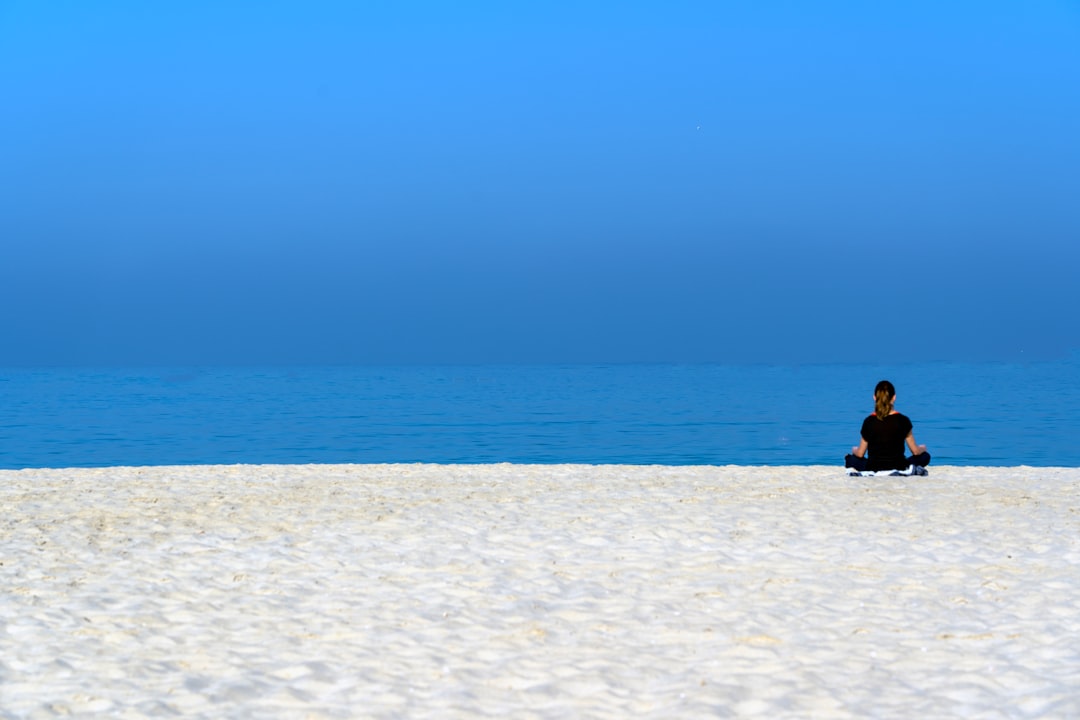 woman in black shirt sitting on white sand during daytime