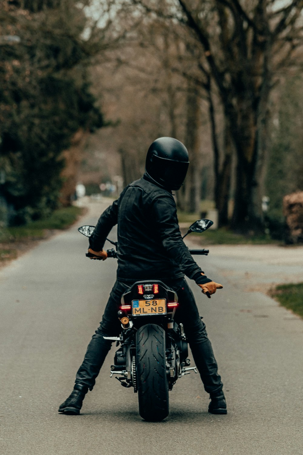 검은 가죽 재킷을 입은 남자가 낮 동안 도로에서 오토바이를 타고