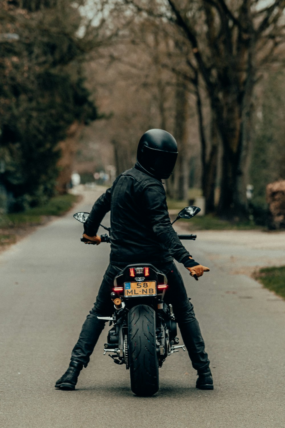 昼間の道路でバイクに乗る黒い革ジャンの男