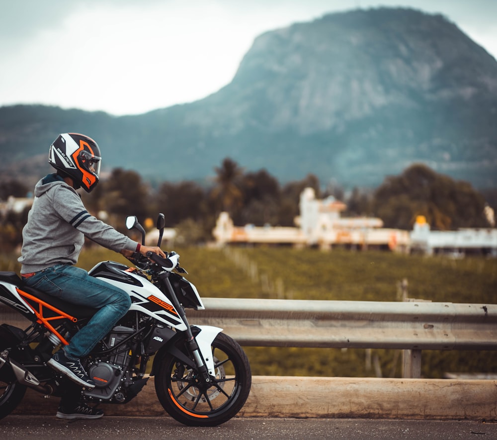 man in blue jacket riding on black and orange sports bike