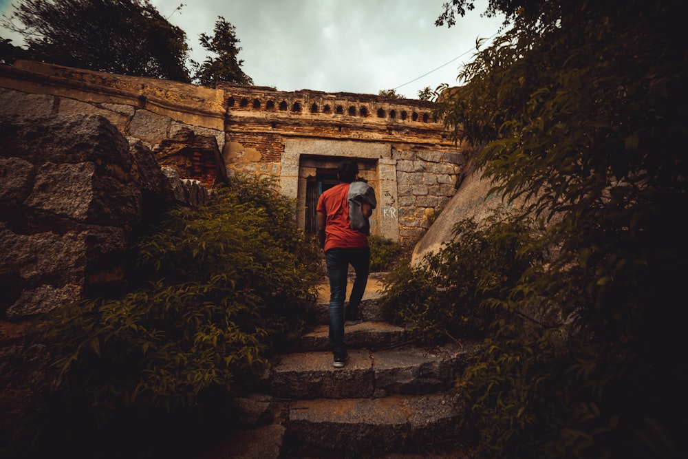 man in red shirt and black pants standing on brown rock formation during daytime