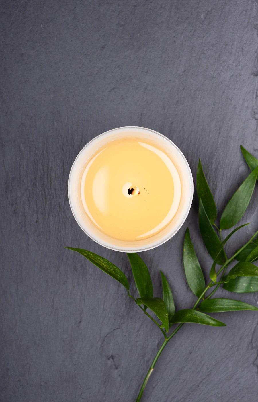 A finished cream candle in a round jar on dark slate with a green sprig
