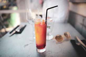 A colorful sensoryta cocktail with layered hues of red and yellow, served in a tall glass with a straw and lemon wedge.