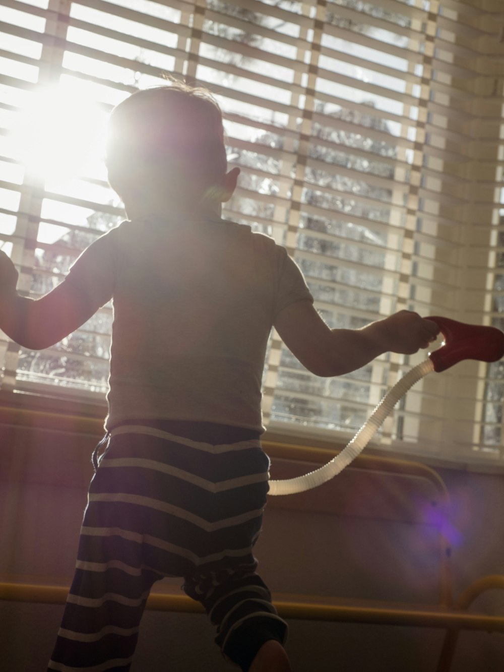 child in brown shirt and black and white striped shorts standing near window