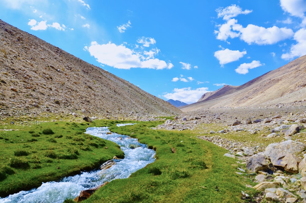 river in between brown mountains under blue sky during daytime